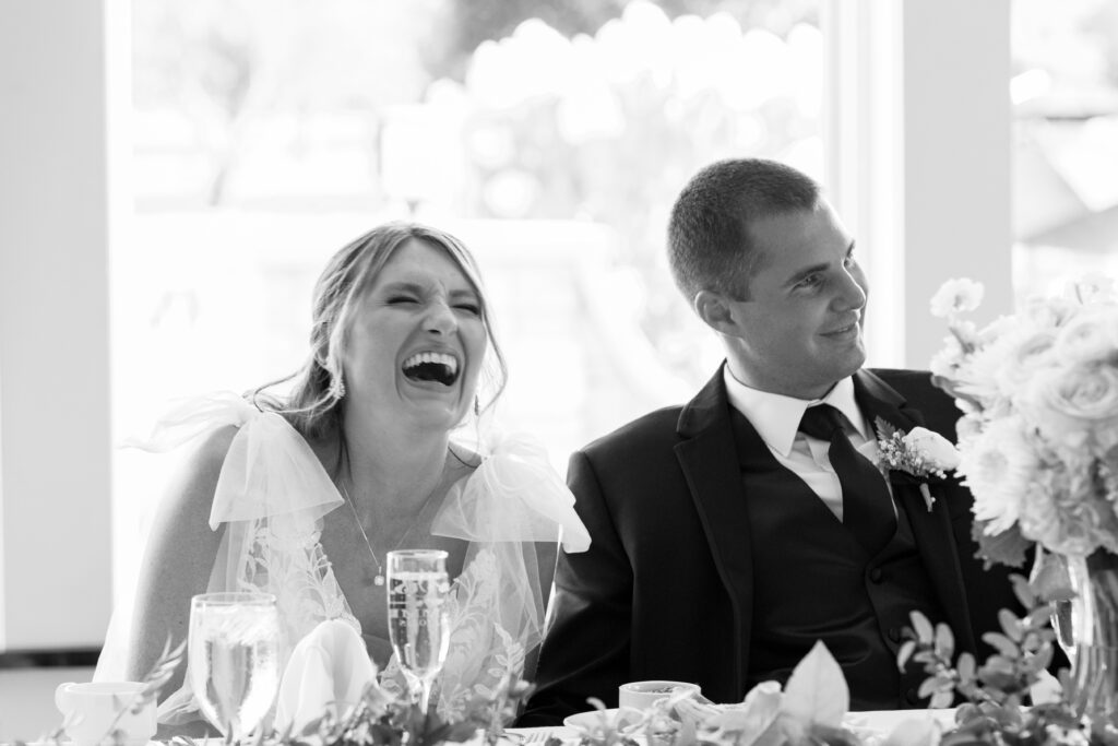 Black and white photo of Bride and groom laughing at the best mans speech. 