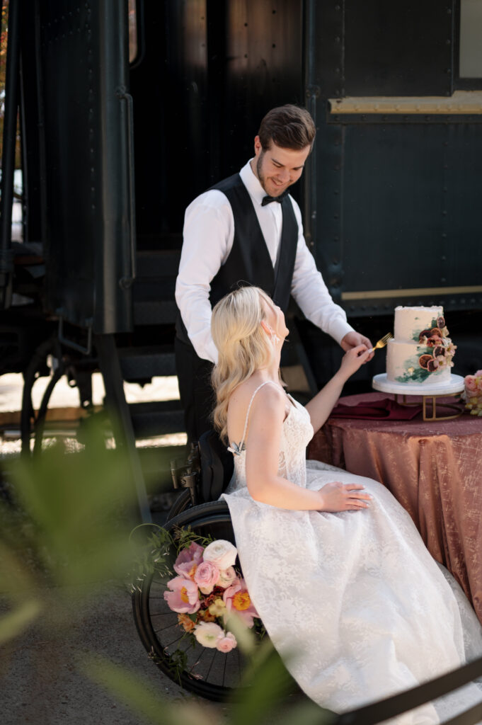 Bride in wheelchair and groom cutting wedding cake outdoors, captured in soft natural light with an elegant, editorial feel